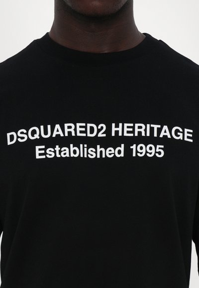 Schwarzes Baumwoll-T-Shirt mit fettem weißen Text: "DSQUARED2 HERITAGE gegründet 1995." Klassisches Rundhalsausschnitt-Design. Glatte Textur.