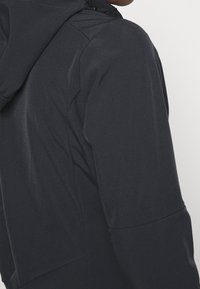 Sudadera oscura y ligera con capucha, que presenta una textura suave, costuras mínimas y una silueta ajustada. Diseño simple y funcional.