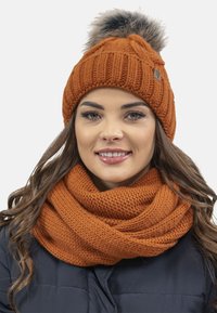 Berretto lavorato a maglia arancione con un motivo testurizzato e un pom-pon in pelliccia sintetica, abbinato a una sciarpa chunky coordinata dello stesso colore.