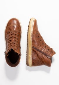 Brązowe skórzane sneakersy w średniej wysokości z sznurowaniem z przodu, bocznym zamkiem, teksturowaną powierzchnią oraz kremową gumową podeszwą. Zawierają kontrastowe detale w szwach.