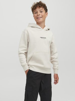 Polo-tröja i ljus beige bomullsblandning med en framficka, justerbar luva med snodd och "Original Studio"-logotyp i svart. Svarta cargobyxor.