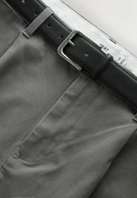 Pantalon gris avec poche avant porté avec une ceinture en cuir noire dotée d'une boucle métallique argentée et une étiquette blanche de marque visible à l'intérieur de la ceinture.