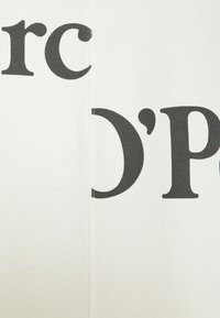 Bílá tkanina s velkým černým nápisem "Marc O'Polo." Hladký povrch s vertikálním švem na jedné straně.