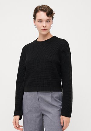 Svart strikket genser med cropped design, rund hals og lange ermer. Stoffet har en subtil vevd struktur.