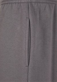 Pantalones de chándal grises con una textura suave, que cuentan con un bolsillo lateral y una cintura elástica para un ajuste cómodo.