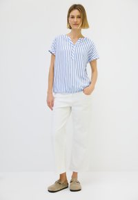 Blusa a maniche corte a righe in blu e bianco, con scollatura a V. Abbinata a pantaloni bianchi a gamba larga e zoccoli beige.