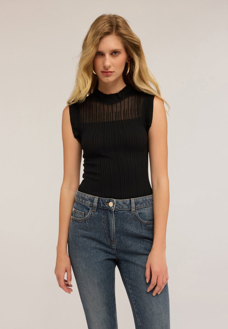 Top senza maniche nero a coste con un pannello a strisce trasparente all'apertura del collo, abbinato a jeans in denim blu a vita alta con tasche frontali.