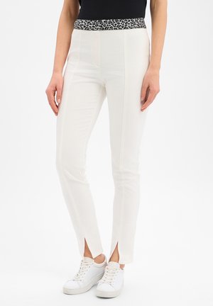 Białe, wąskie spodnie z przednimi szwami i małymi rozcięciami przy kostkach, z paskiem w panterkę, noszone z białymi trampkami i czarnym topem.