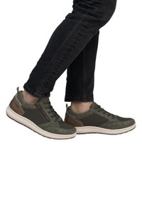 Green athletic shoes with mesh panels, suede accents, and a rubber sole. Features a lace-up design and a side zipper detail.