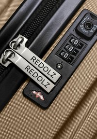 Reisetasche mit beiger strukturierten Oberfläche, silbernen Doppelreißverschlüssen, die mit "REDOLZ" gekennzeichnet sind, und einem schwarzen Kombinationsschloss.