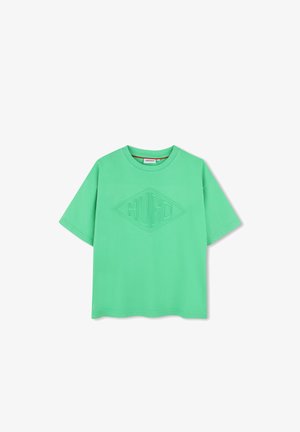 Camiseta de algodón verde con un corte relajado, que presenta un logo texturizado en forma de diamante en el centro. Cuello redondo y mangas cortas.