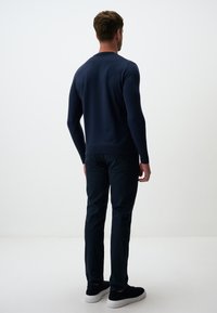 Maglione lavorato a maglia blu navy con collo a giro e silhouette aderente, abbinato a pantaloni scuri e scarpe nere. Tessuto liscio, dettagli minimalisti.