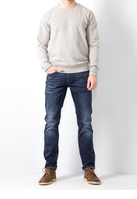 Sudadera gris con cuello redondo, combinada con jeans de mezclilla azul oscuro de corte recto. Zapatos de ante marrón con cordones.