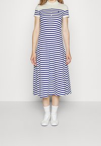 Pasiasta sukienka polo w białym i granatowym kolorze, do kolan, z kołnierzykiem i krótkimi rękawami. Połączona z białymi trampkami i skarpetkami.