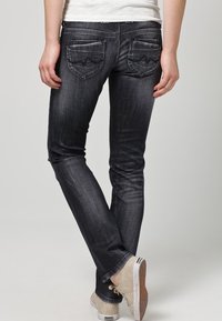 Vaqueros de mezclilla de lavado oscuro con un corte ajustado, que presentan costuras en contraste y bolsillos traseros decorativos con un patrón en zigzag.