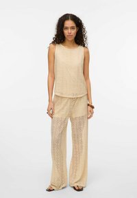 Beige kanten tanktop en wijde broekset met cirkelvormige patroon overlays. Losse pasvorm, lichte textuur en transparante uitstraling.