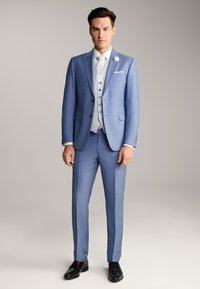 Costume bleu clair avec une finition texturée, gilet blanc et cravate. Les détails notables incluent une fleur à revers et des chaussures noires brillantes.