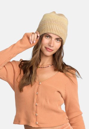 Beige Strickmütze mit geripptem Muster, kombiniert mit einem hellorangenen, gerippten Croptop mit Knöpfen und langen Ärmeln.