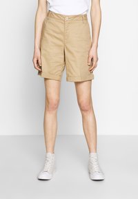 Beiga bomullsshorts med vikbar fåll, med framknäppning och sidofickor, kombinerade med vita högsneakers.