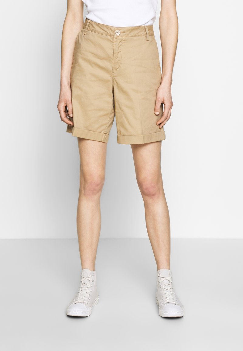 Beiga bomullsshorts med vikbar fåll, med framknäppning och sidofickor, kombinerade med vita högsneakers.