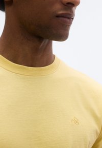Κίτρινη βαμβακερή μπλούζα με στρογγυλή λαιμόκοψη και διακριτικό ανάγλυφο λογότυπο στο στήθος. Λεπτή υφή με ελαφριά εμφάνιση.