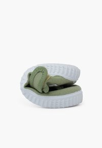 Zapatillas de lona verdes con parte superior acolchada, suela de goma blanca y patrón de textura en la suela. El diseño presenta una estructura doblada.