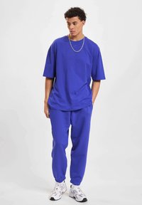 Koninklijk blauwe oversized t-shirt met korte mouwen, gecombineerd met bijpassende smal gesneden sweatpants en witte sportschoenen. Eenvoudig ontwerp en zachte textuur.