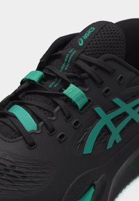 Μαύρο αθλητικό παπούτσι Asics με τόνους τιρκουάζ, γλώσσα από δίχτυ και κορδόνια, που αναδεικνύει το λογότυπο της μάρκας και τις υφασμάτινες λεπτομέρειες της υφής.