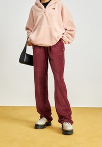 Rosa fleecehoodie med framficka och halvdragkedja, ihopparad med vinröda kordbyxor. Vita klumpiga skor fulländar outfiten.