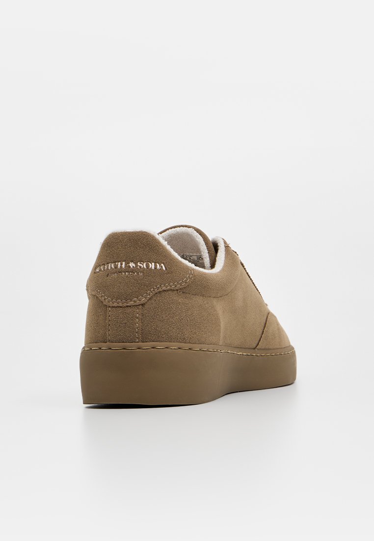 Brązowe zamszowe trampki z gumową podeszwą, wyściełanym kołnierzem i nosem w kształcie migdała. Posiadają zdobienia w postaci szwów oraz logo na pięcie.