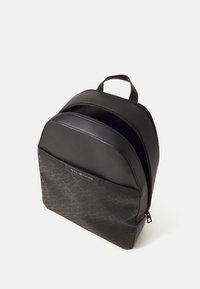 Sac à dos noir en matériau synthétique lisse avec un devant texturé et à motifs. Il comprend une poignée supérieure et des compartiments zippés.