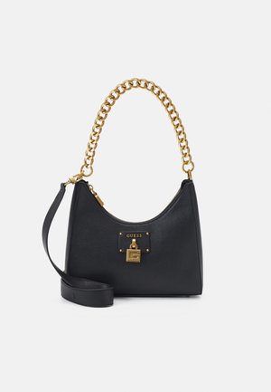 Sac à main en cuir noir avec anse en chaîne dorée, détail de cadenas doré, et bandoulière noire amovible, marqué "GUESS" à l'avant.