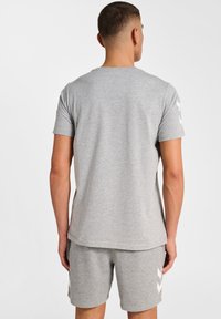 Grå bomulls T-skjorta med kort ärm; enfärgad; har vita chevrondetaljer på axlarna; avslappnad passform; rundad halsringning.