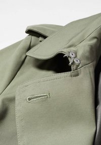 Gros plan du col d'une veste vert olive avec des coutures détaillées, une boutonnière et deux boutons métalliques avec fermeture à crochet.
