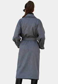 Szary płaszcz wełniany, o średniej długości, z paskiem w talii, szerokimi rękawami, miękką teksturą, widocznymi detalami szwów, minimalistycznym designem, bez wzorów czy akcentów.