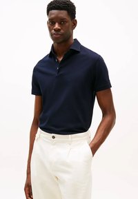 Polo shirt blu navy con colletto classico e tre bottoni, realizzato in tessuto liscio. Indossato con pantaloni di colore chiaro.