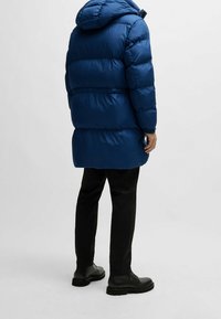 Blue puffer coat with hood, featuring quilted sections and a shiny texture. Paired with black pants and black boots.