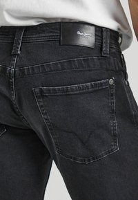 Černé džíny z nekteré látky s úzkým střihem, disponující klasickým designem pěti kapes, jemným prošíváním a koženým logem na pasu.