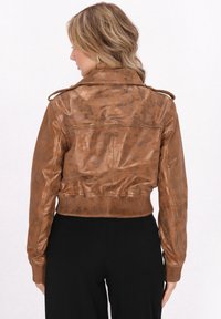 Brun læder cropped jakke med ribbede manchetter og kant, der har en let glat overflade og skulderepaulettes.