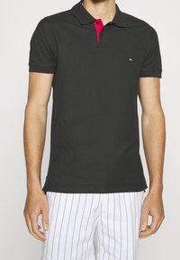 Svart polo skjorta med röd knappad krage, med en liten logotyp på vänster bröst; mjukt tyg och korta ärmar.