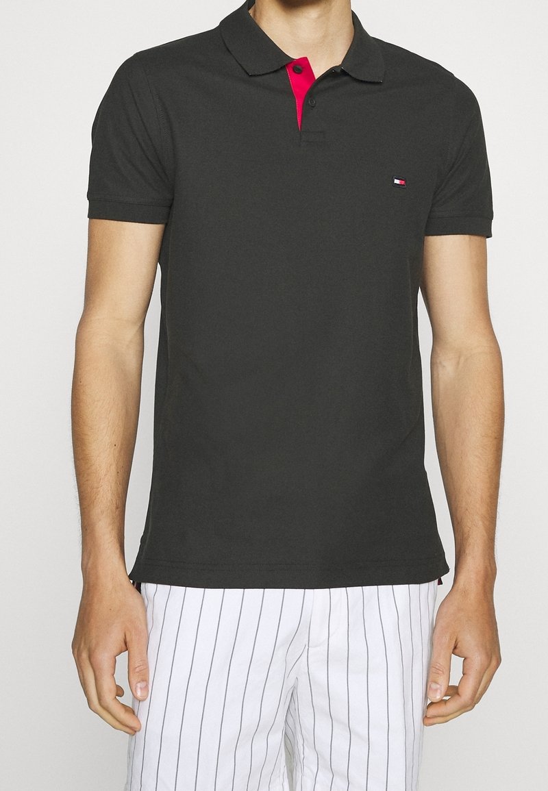 Svart polo skjorta med röd knappad krage, med en liten logotyp på vänster bröst; mjukt tyg och korta ärmar.