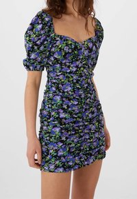 Blommig mini-klänning i svart tyg, med lila och gröna blommönster, puffärmar, fyrkantig halsringning och rynkade detaljer genom hela klänningen.