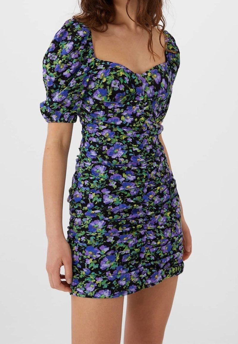 Blommig mini-klänning i svart tyg, med lila och gröna blommönster, puffärmar, fyrkantig halsringning och rynkade detaljer genom hela klänningen.