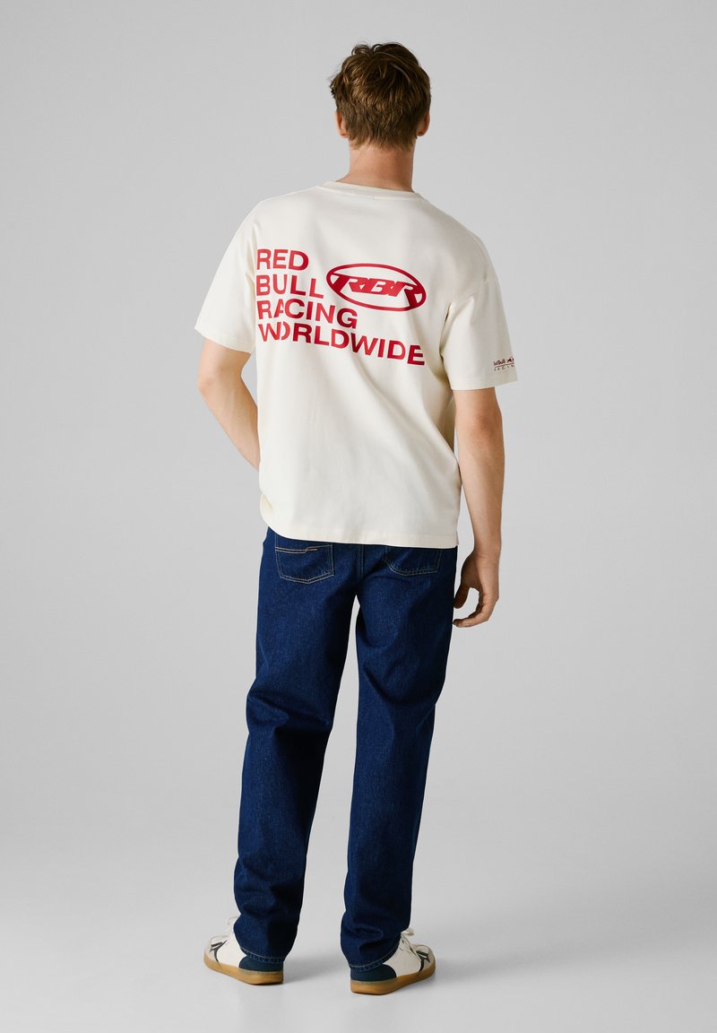 Hvid bomulds t-shirt med fed rød tekst: "RED BULL RACING WORLDWIDE." Sammen med blå denim jeans, afslappet pasform, og hvide sneakers.