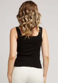 Haut noir sans manches avec des bords festonnés, design ajusté et une finition texturée, associé à un jean clair.