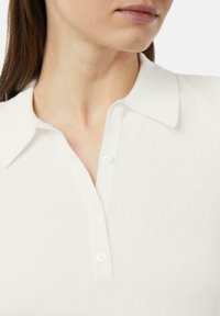 Biała polo z prążkowanej tkaniny z kołnierzykiem, trzema guzikami z przodu i gładką fakturą. Zbliżenie podkreśla detale tkaniny.