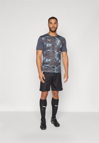 Black soccer shorts with a black and blue patterned short-sleeve jersey featuring a round neckline and logo on the chest; black socks and cleats.