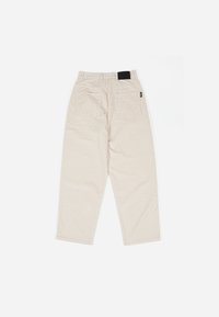 Beige corduroy pants with a relaxed fit, featuring two back pockets and a black waistband label. Textured fabric with vertical ribbing.
