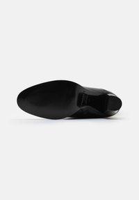 Semelle de chaussure en cuir noir avec une surface lisse et un motif de texture striée. Bout arrondi et petit talon, présentant un détail de marque près du talon.