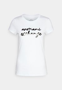 Camiseta de algodón blanca con un estampado en negro metálico que dice "armani exchange" en un estilo casual y manuscrito. Cuello redondo.